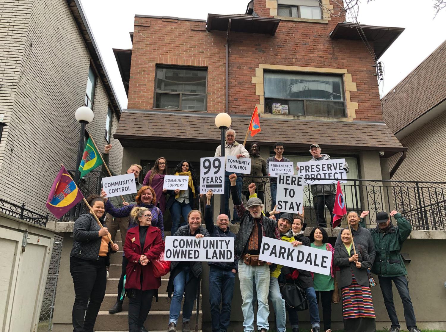 Photograph of members of the Parkdale community land trust holding protest posters outside of one of their properties.